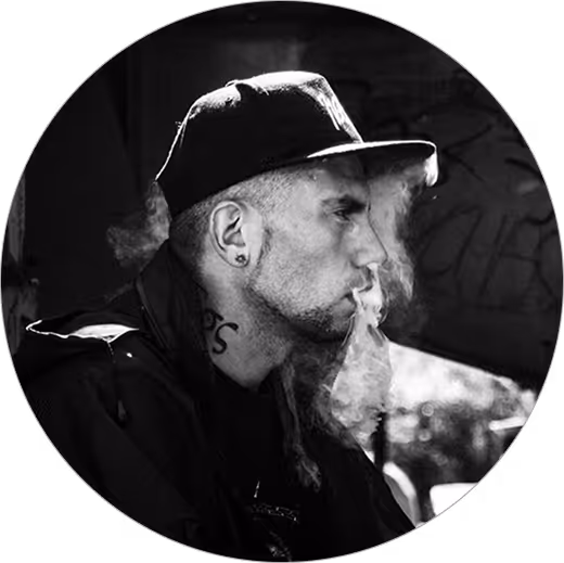 Black and white profile of a man wearing a cap, smoking with visible vapor around his face.